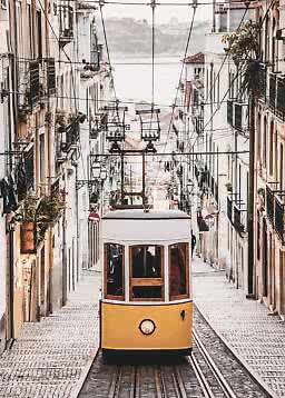 Yellow tram on a steep cobblestone street between narrow buildings and overhead wires