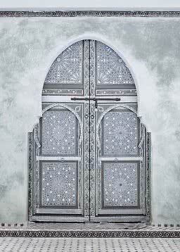 Ornate double door with geometric patterns set in a white arched wall