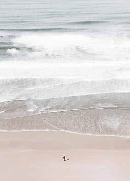Eine Person steht allein an einem hellen Sandstrand vor großen Wellen