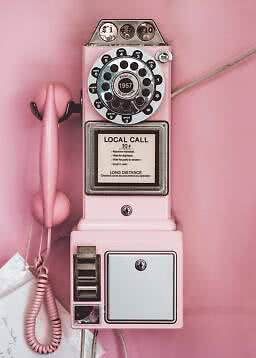 Teléfono público retro rosa con disco giratorio y auricular en una pared rosa