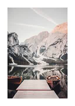 Wooden dock with two rowboats on a calm mountain lake, with snowy cliffs reflected in the water
