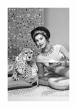 Black-and-white photo of an elegant woman with a drink beside a cheetah and beaded curtain
