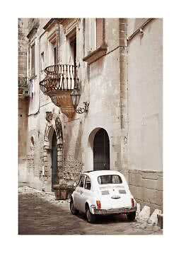 White vintage car parked on a narrow cobblestone street beside an old stone building with balcony