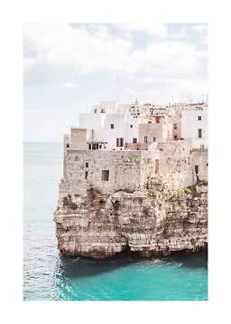 White and stone houses on a cliff above turquoise sea under a bright sky