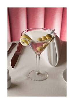 Martiniglas mit klarem Cocktail, grünen Oliven und Zitronenzeste auf gedecktem Tisch vor rosa Hintergrund