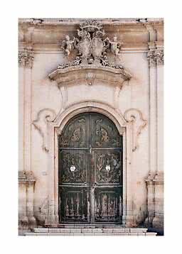 Ornate Baroque doorway in pale stone with dark weathered double doors and sculptures above