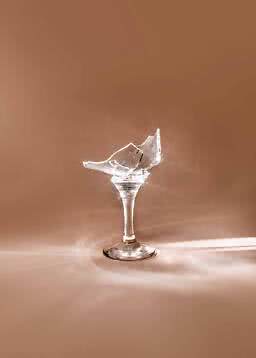 Zerbrochenes Cocktailglas mit Stiel vor beigem Hintergrund mit funkelnden Lichtreflexen