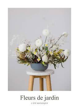 Blomsterarrangemang med vita blommor och gula detaljer i grå skål på en träpall