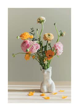 Bouquet di fiori rosa, gialli e crema in un vaso bianco a forma di corpo, su tavolo con petali