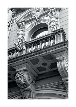 Black-and-white photo of ornate facade with balcony, arched window and classical statues