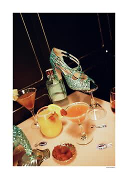 Sandalo con tacco turchese glitterato su un bicchiere da cocktail con drink e gioielli