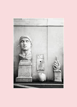 Foto in bianco e nero di sculture antiche in marmo contro un muro, con grande testa e mano