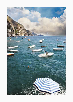Coastal scene with small boats on the sea, cliffs on the left, and a blue sky with large clouds