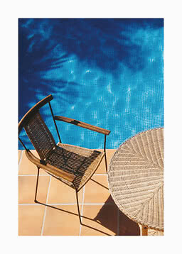 Woven chair and round table on tiled patio beside a blue swimming pool