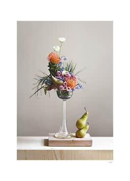 Blumenarrangement in hoher Glasvase mit bunten Blumen und zwei Birnen auf Holzblock