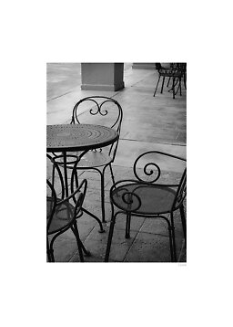 Foto en blanco y negro de mesa y sillas de hierro forjado en un patio con baldosas