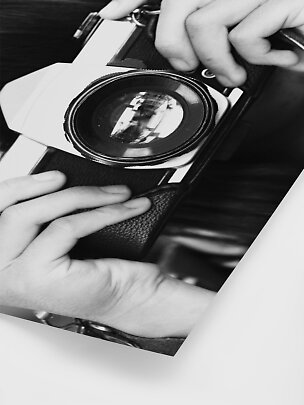 Primo piano in bianco e nero di mani che tengono una fotocamera vintage con grande obiettivo