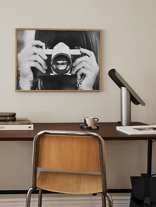 Scrivania con sedia in legno, lampada da tavolo e foto in bianco e nero incorniciata con fotocamera