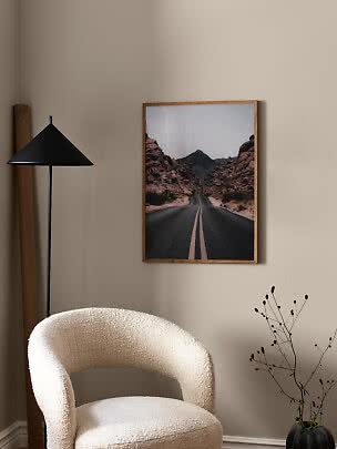 Indrammet plakat med ørkenvej mellem klipper hænger på beige væg i stue