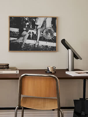 Wooden desk with chair, lamp, cup, and framed black-and-white photo on the wall