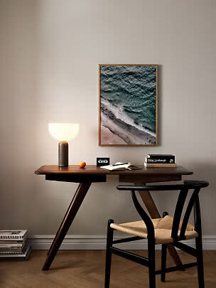 Dark wooden desk with glowing table lamp, chair, and framed ocean print on the wall