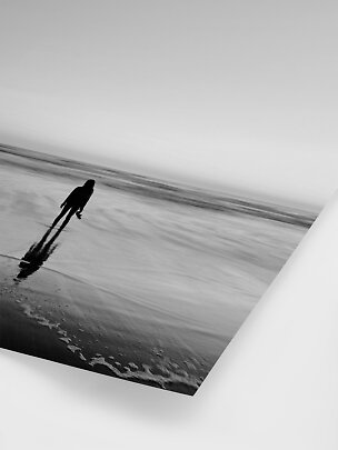 Photo en noir et blanc d’une personne sur la plage, reflet dans le sable mouillé