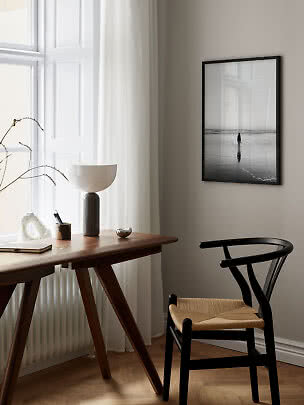 Espace de travail minimaliste avec bureau en bois, chaise noire et photo de plage en noir et blanc