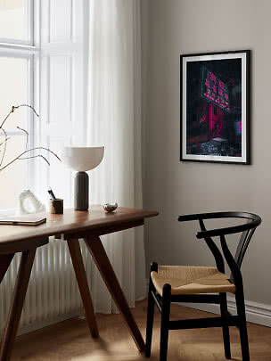 Indrammet plakat med neonoplyst bygning hænger over skrivebord i lyst, moderne rum