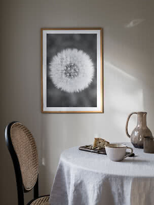 Affiche encadrée noir et blanc de pissenlit au mur au-dessus d’une table avec tasse et gâteau
