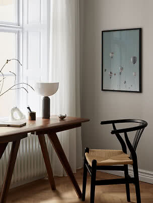 Minimalistische werkplek met houten bureau, zwarte stoel, tafellamp en ballonposter bij het raam