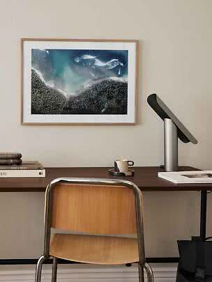 Schreibtisch mit Holzstuhl, schwarzer Tischlampe und gerahmtem Küstenbild an der Wand