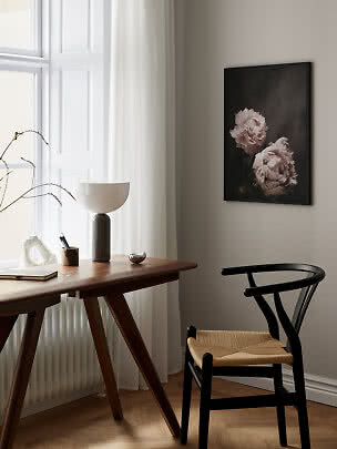 Rincón de escritorio con silla negra, lámpara de mesa y cuadro floral en la pared
