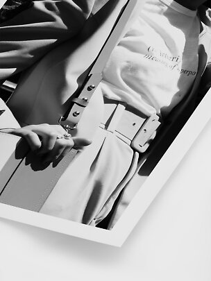 Black-and-white fashion photo of a person in blazer, slogan T-shirt, belt and shoulder bag.