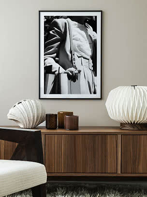 Framed black-and-white fashion photo above a wooden sideboard with lamp, shell decor and glass holders