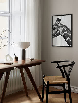Schwarz-weißes Giraffenbild im schwarzen Rahmen über einem Holztisch neben einem hellen Fenster