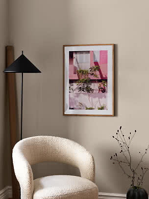 Framed print of a pink building and plants on a beige wall above a cream armchair