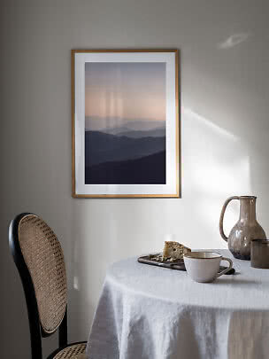 Gerahmtes Poster mit geschichteten Bergsilhouetten in sanften Tönen an der Wand über einem Tisch