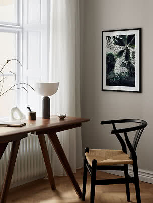 Framed botanical print on wall above a wooden desk and black chair by a bright window