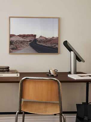 Skrivebord med stol, lampe og indrammet ørkenlandskab med snoet vej på væggen