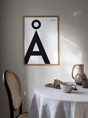 Ingelijste typografische poster met de letter Å aan lichte muur boven een gedekte tafel