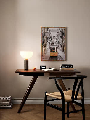 Home office with dark wood desk, black chair, lit table lamp and framed tram print on the wall