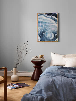 Bedroom with blue bedding, dark side table, vase with branches, and abstract blue wall art
