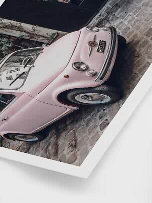 Pink vintage car parked on a cobblestone street, viewed from the front at an angle