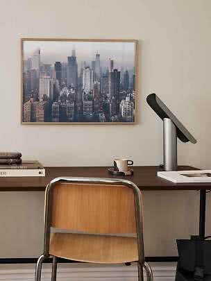 Schreibtisch mit Stuhl, schwarzer Lampe und gerahmtem Stadtbild an der Wand