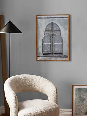 Framed print of an ornate arched doorway on a gray wall above a cream textured armchair