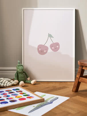 White-framed kids poster with two pink smiling cherries, leaning against the wall
