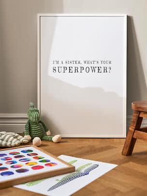 Weiß gerahmtes Poster mit dem Text "I'm a sister, what's your superpower?" auf dem Boden im Kinderzimmer.