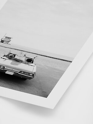 Black-and-white photo print of a convertible by the beach with a surfboard and people