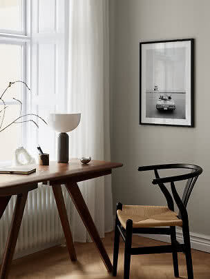 Minimalist home office with wooden desk, black chair, table lamp and framed black-and-white photo.
