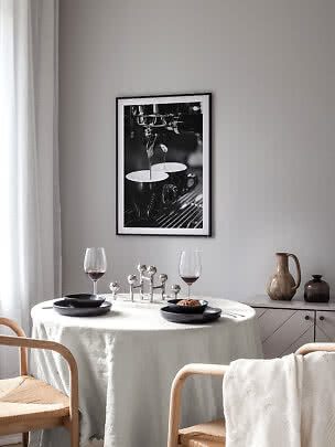 Angolo pranzo con tavolo rotondo, piatti neri, calici da vino e foto caffè in bianco e nero